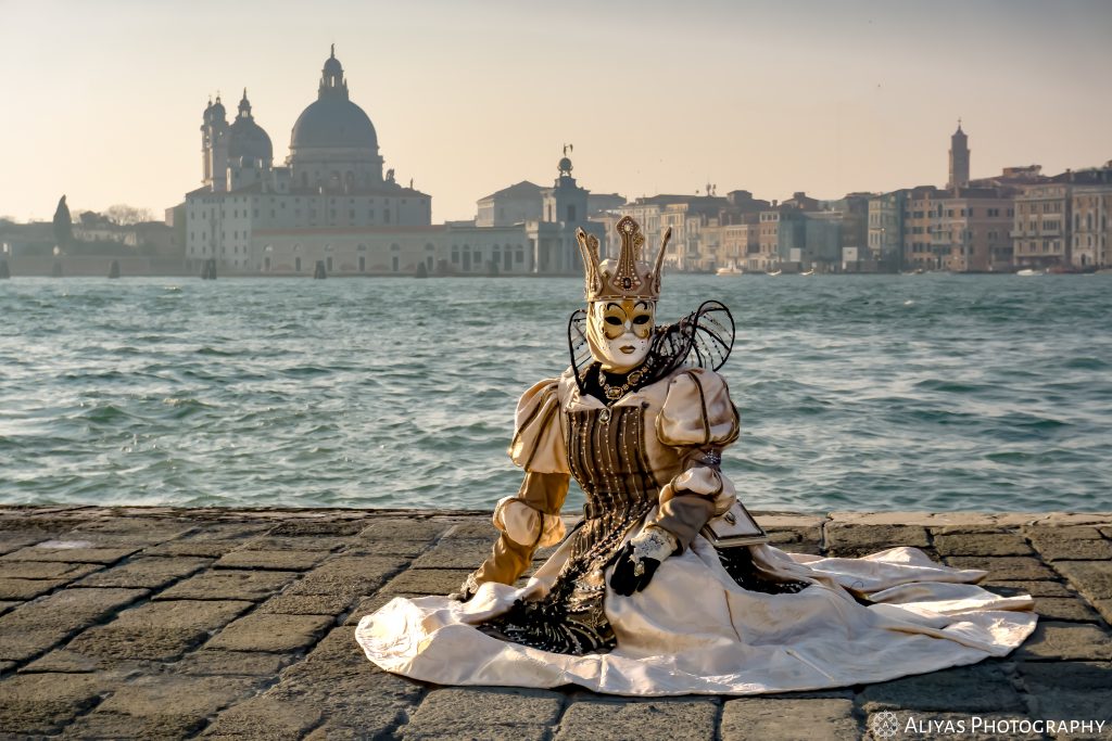On this picture, you can see a woman lying on the ground and wearing a white-golden-black costume in the Carnival of Venice 2019. She wears a golden crown.