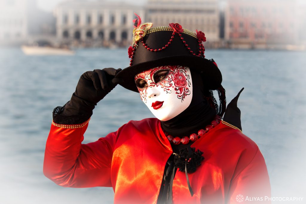 On this picture, you can see a woman wearing a red and black costume in the Carnival of Venice in 2019. Her accessory is a black hat covered with red roses and chains.