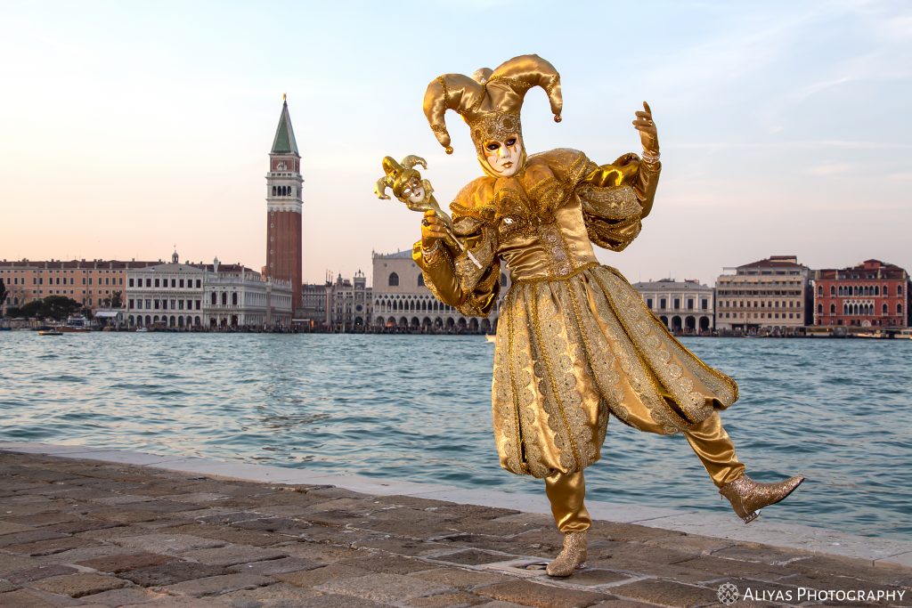 On this picture, you can see a man wearing a golden joker costume in the Carnival of Venice in 2019. His accessory is a mini golden mask attached to a stick which is a copy of his white golden mask.