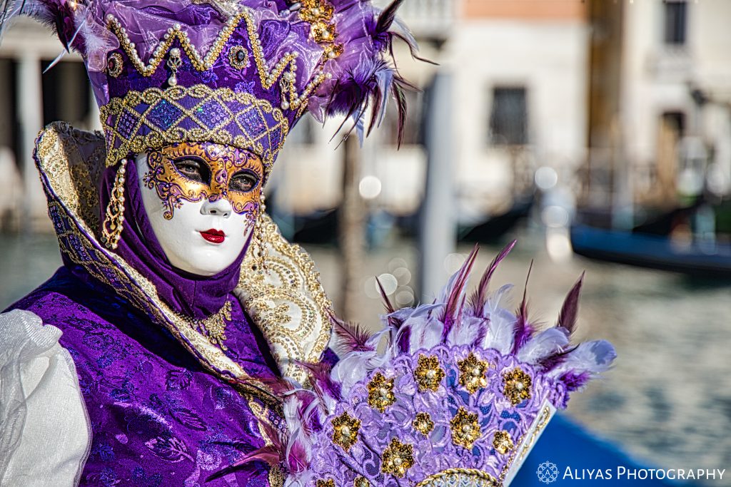 On this picture, you can see a woman wearing a lilac costume in the Carnival of Venice in 2020. Her accessory is a lilac fan.