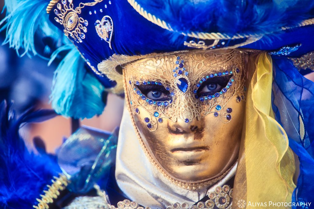On this picture, you can see a woman wearing a black and gold costume in the Carnival of Venice in 2020. Her golden mask is ornated with blue crystals.