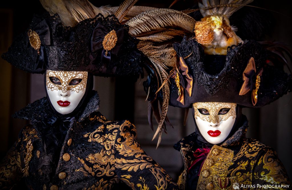 On this picture, you can see two women wearing elaborate golden-black costumes in the Carnival of Venice 2018. One of the women wears a hat with a golden chicken on it.